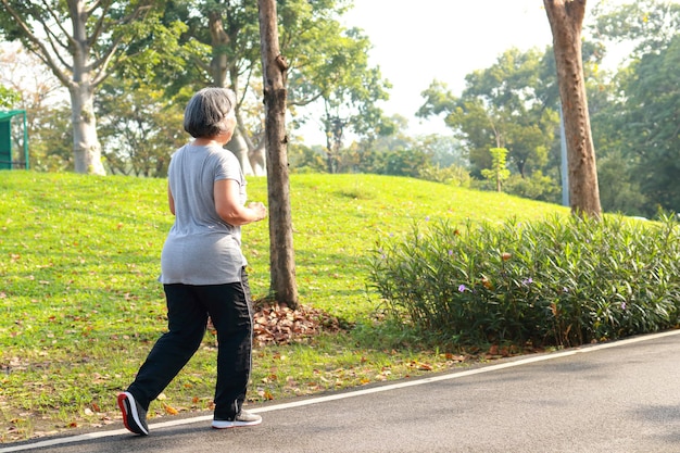 Asian elderly woman jogging in the park in the morning she smiles happy Healthy body. concept of health care for seniors to be healthy. Copy space