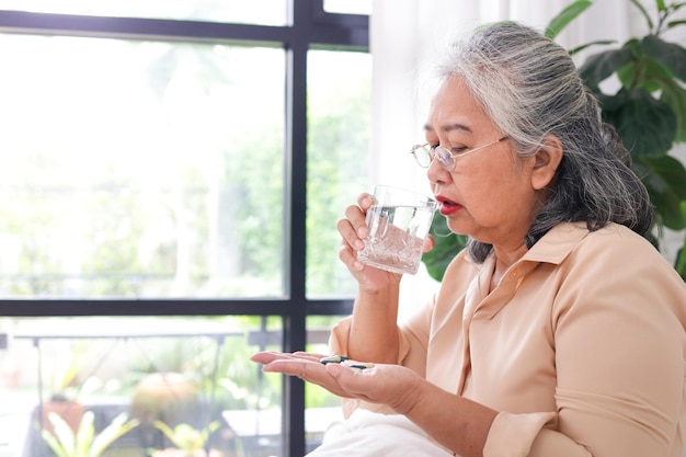 Asian elderly woman stay at home She has a flu She is taking painkillers and drinking plain water The concept of disease of the elderly Caring for the elderly during COVID19