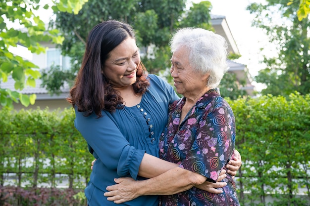 Asian elderly woman with caregiver walking help with love and happy in nature park.