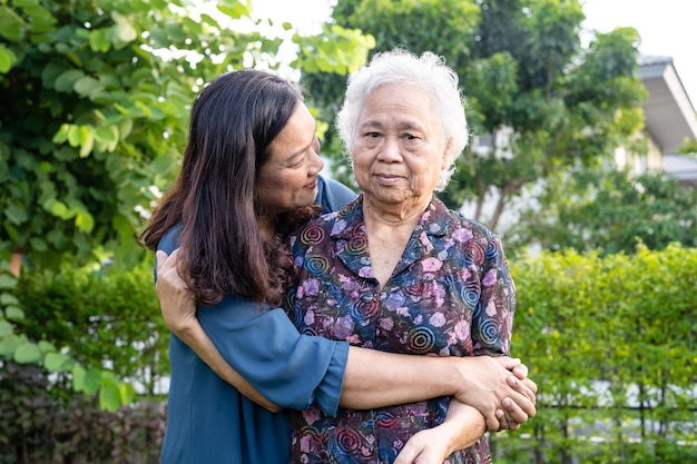 Asian elderly woman with caregiver walking with happy in nature park.