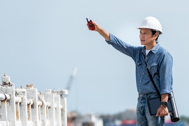 Asian engineer man standing on the dock Holding walkie talki tablet Compare with real locations