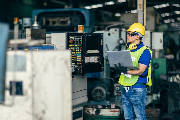 Asian engineer programming the machine in factory with laptop computer to setup program process.