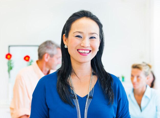 Asian ethnic woman smiling at the camera with two caucasians in the background.