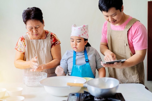 Asian families are helping each other in cooking daughter father and grandmother Dad uses a tablet to see how to cook