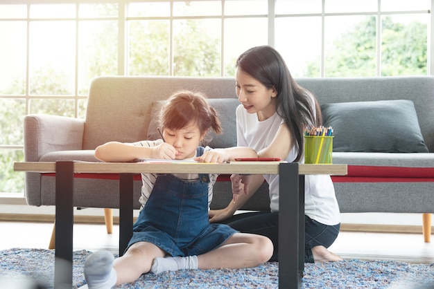 Asian family mother and little girl learning and writing in book with pencil making homework.