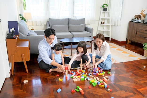 Asian family with children playing and building tower of colorful wooden toy blocks in living room