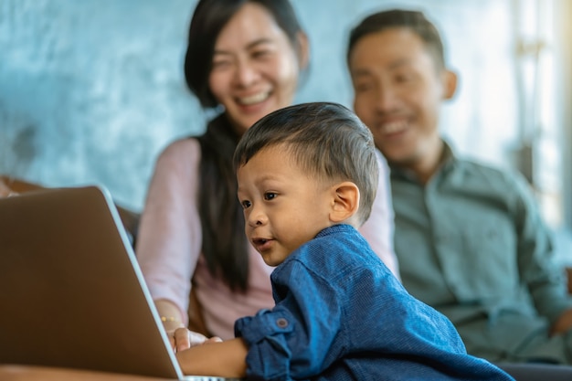 Asian family with son are looking the cartoon via technology laptop and playing together