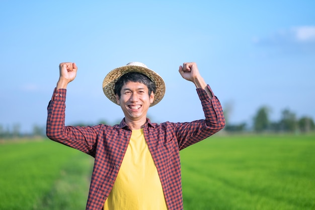 Asian farmer man smile face and raised hands looking at a green rice farm.