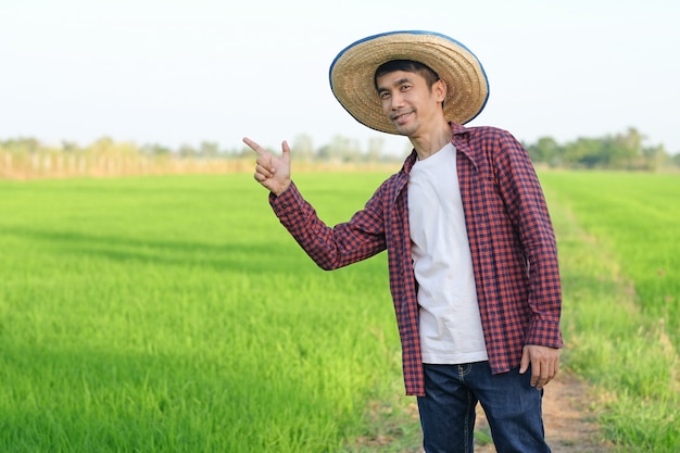 Asian farmer man smile and raise hand point to side at green rice farm