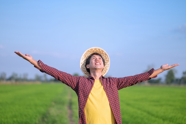 Asian farmer man smile and raised hands looking at a green rice farm