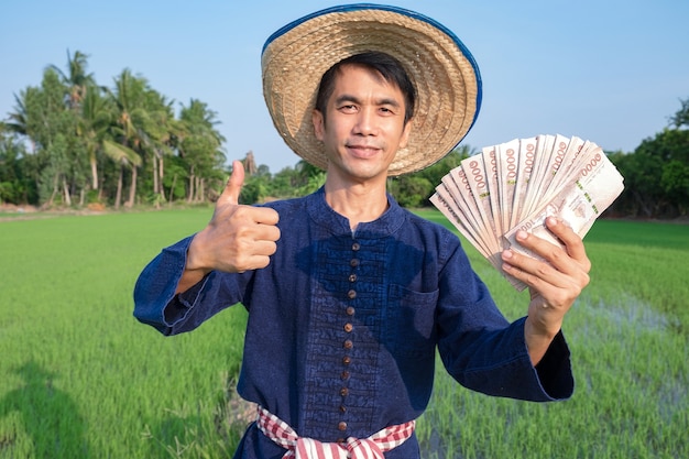 Asian farmers wear traditional costume shirts holding Thai banknote money at the green farm.