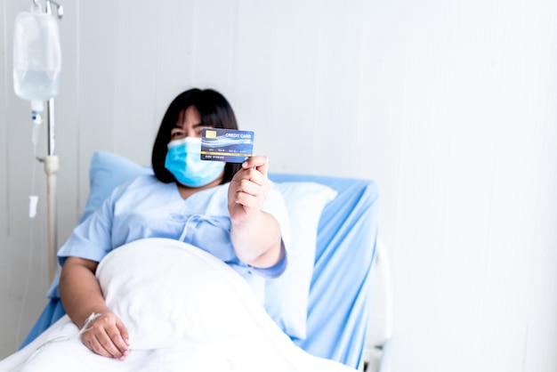 Asian fat woman patients wearing a masks sitting in a patients bed Show mock up credit card