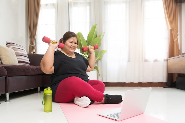 Asian fat woman workout at home with using laptop computer learning virtual internet online, Sport exercising weight loss and recreation idea concept.