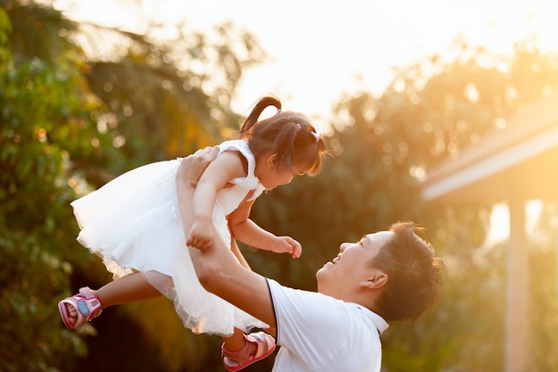 Asian father carrying his daughter up in the air and playing together in the park