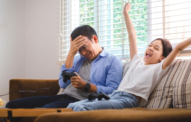 Asian father and daughter playing video games at home People doing activities and family concepts