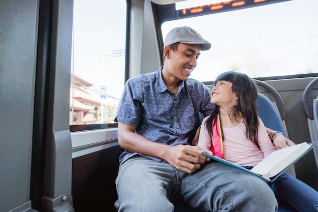 Asian father taking his daughter to school by riding bus public transport and studying