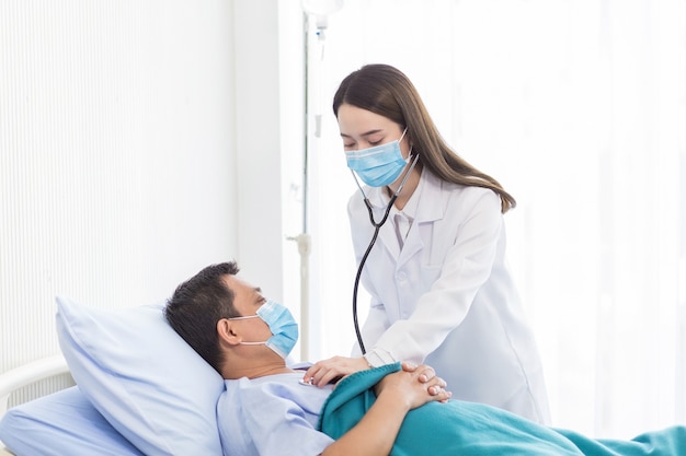 An Asian female doctor examining a man in a hospital bed for a checkup