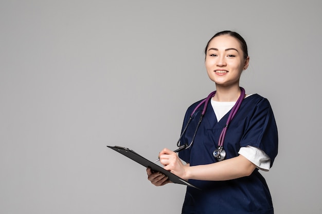 Asian female doctor holding pen writing something on clipboard on white wall