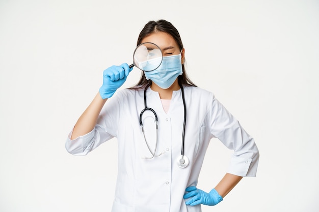 Asian female doctor looking through magnifying glass examine patient searching disease wearing medic...