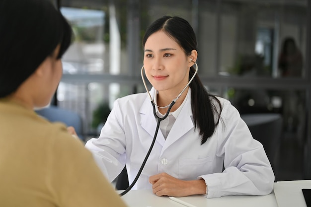 Asian female doctor using stethoscope to listen to patient's heart and lungs sounds