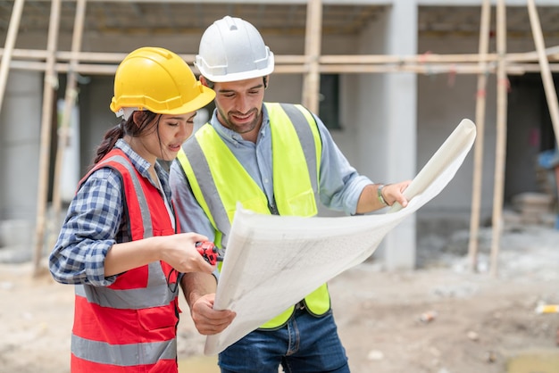 Asian female engineer and male architect discuss and look at blueprints at construction site