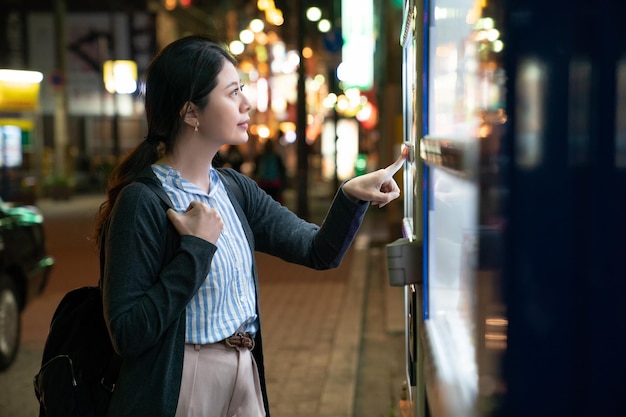 asian female looking for what to drink. standing in front of a vending machine.