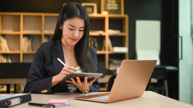 Asian female manager holding stylus pen writing information on digital tablet