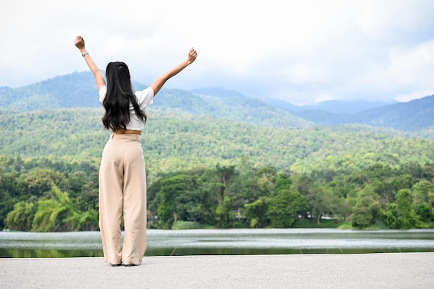 Asian female raising hands with freedom expression standing by the lake with mountain view