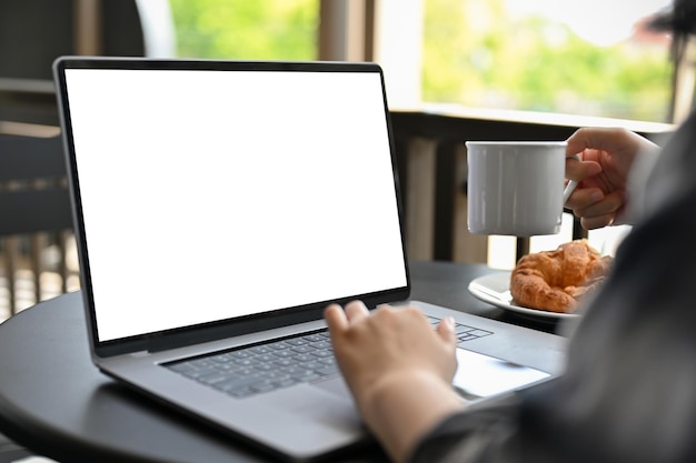 An Asian female remote working at the coffee shop sipping coffee while working on laptop