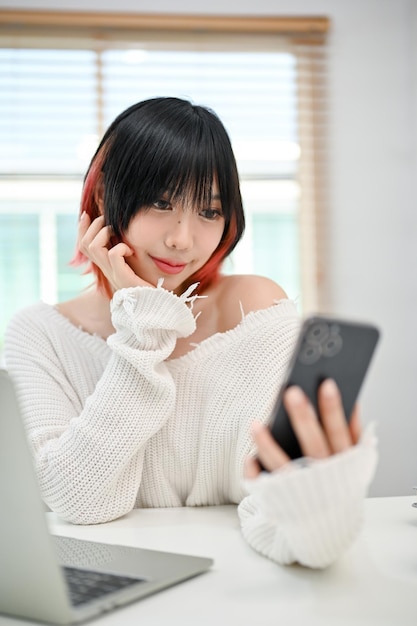 An Asian female taking her picture or selfie with her smartphone while sitting at her desk