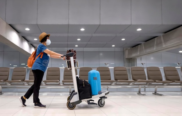 Asian female tourist wearing face mask is walking in airport terminal with luggage during pandemic