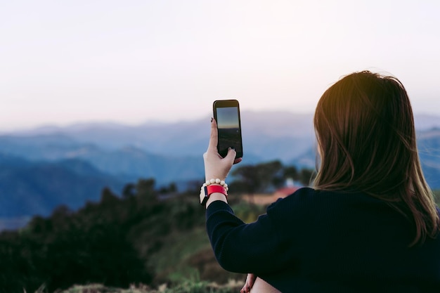 Asian female tourists use their mobile phones to take pictures of the scenery at the top of a fresh mountain hill