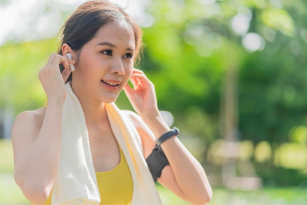 Asian female woman sportwear doing morning jogging holding headphones Putting earphones before exercise Happy young woman listening music outdoors in city park garden morning fitness healthy life