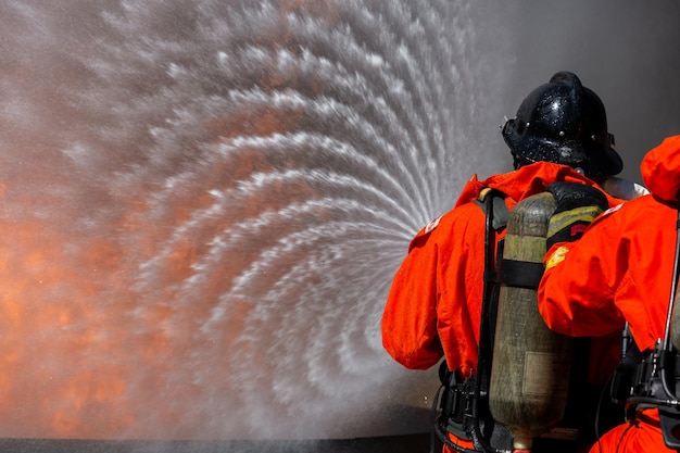 Asian firefighter on duty firefighting Asian fireman spraying high pressure water Fireman in fire fighting equipment uniform spray water from hose for fire fighting