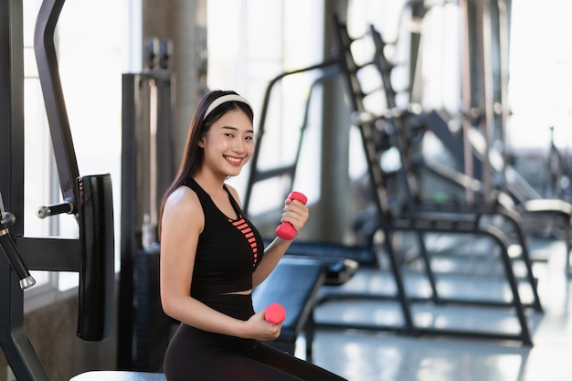 Asian fit sportswoman smiling and working out excercise weights with dumbbells at the fitness gym asian woman wearing sportwear doing exercise to burn fat at gym Sport woman fitness concept