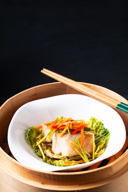 Asian food concept Chinese Steamed fish with ginger and soy sauce in bamboo steamer on black slate stone board with copy space