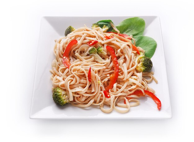 Asian food plate isolated at white background. Vegetarian stir fry with noodles served on square platter and green spinach leaves decoration