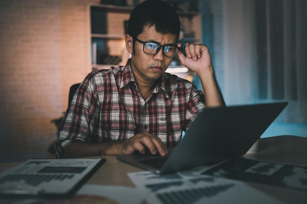 Asian freelance man having stressful depression sad time working on laptop home night Depression man sad serios working from home Man wearing plaid shirt red is rushing work overtime for deadline