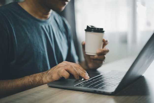 Asian freelance man holding cup of hot coffee and working on laptop computer on wooden table at cafe Entrepreneur woman working for her business at coffee shop Business work from anywhere