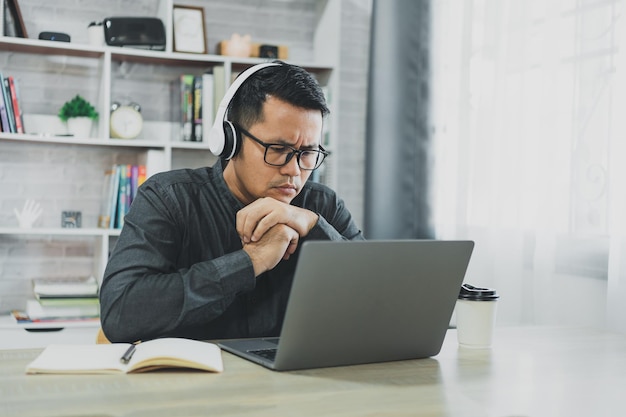 Asian freelance man wear glasses and headphone having stressful depression sad time while working video conferrence meeting on laptop Depression man sad serios working at home Work anywhere concept