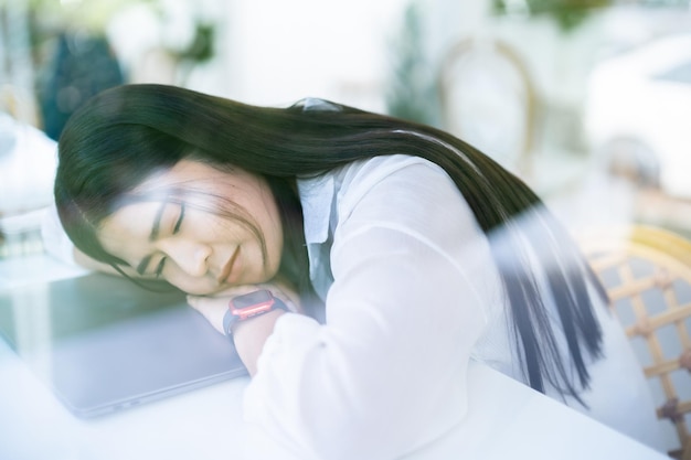 Asian freelance people business female wearing smartwatch fell asleep using after working with laptop computer for browsing internet chatting and blogging and smartphonenotebook in coffee shop