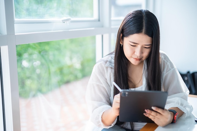 Asian freelance people business female wearing smartwatch talking making using casual working with tablet for browsing internet chatting and blogging and smartphonenotebook in coffee shop