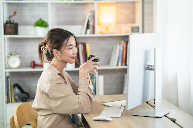 Asian freelance woman smiling holding cup of hot coffee and working on laptop computer on wooden table at home Entrepreneur woman working for her business at home Business work at home concept