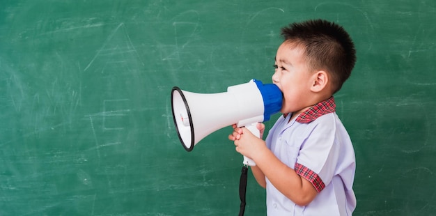 Asian funny little boy kindergarten preschool in student uniform speaking through megaphone against