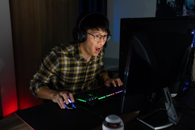 asian gamer guy in headphones enjoy and rejoicing while playing video games on computer