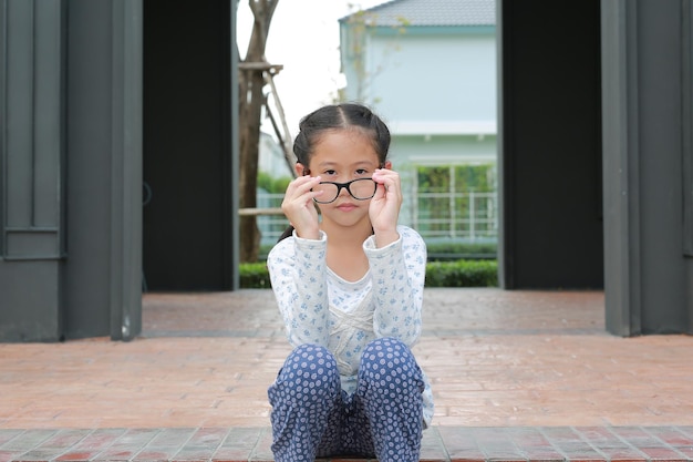 Asian girl child sitting in the garden while take off glasses and looking at camera