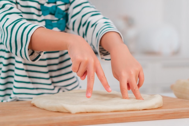 Asian girl having fun using finger to knead the dough and preparing bakery in the kitchen.