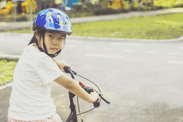 Asian girl learns to ride bike in park. Portrait of a cute kid on bicycle.