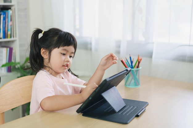 Asian girl looking and touch on white screen at the tablet screen attentively overstimulated children concept Too much screen time Cute girl watching videos while tv Internet addiction concept