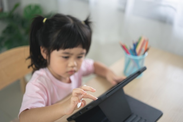 Asian girl looking and touch on white screen at the tablet screen attentively overstimulated children concept Too much screen time Cute girl watching videos while tv is working